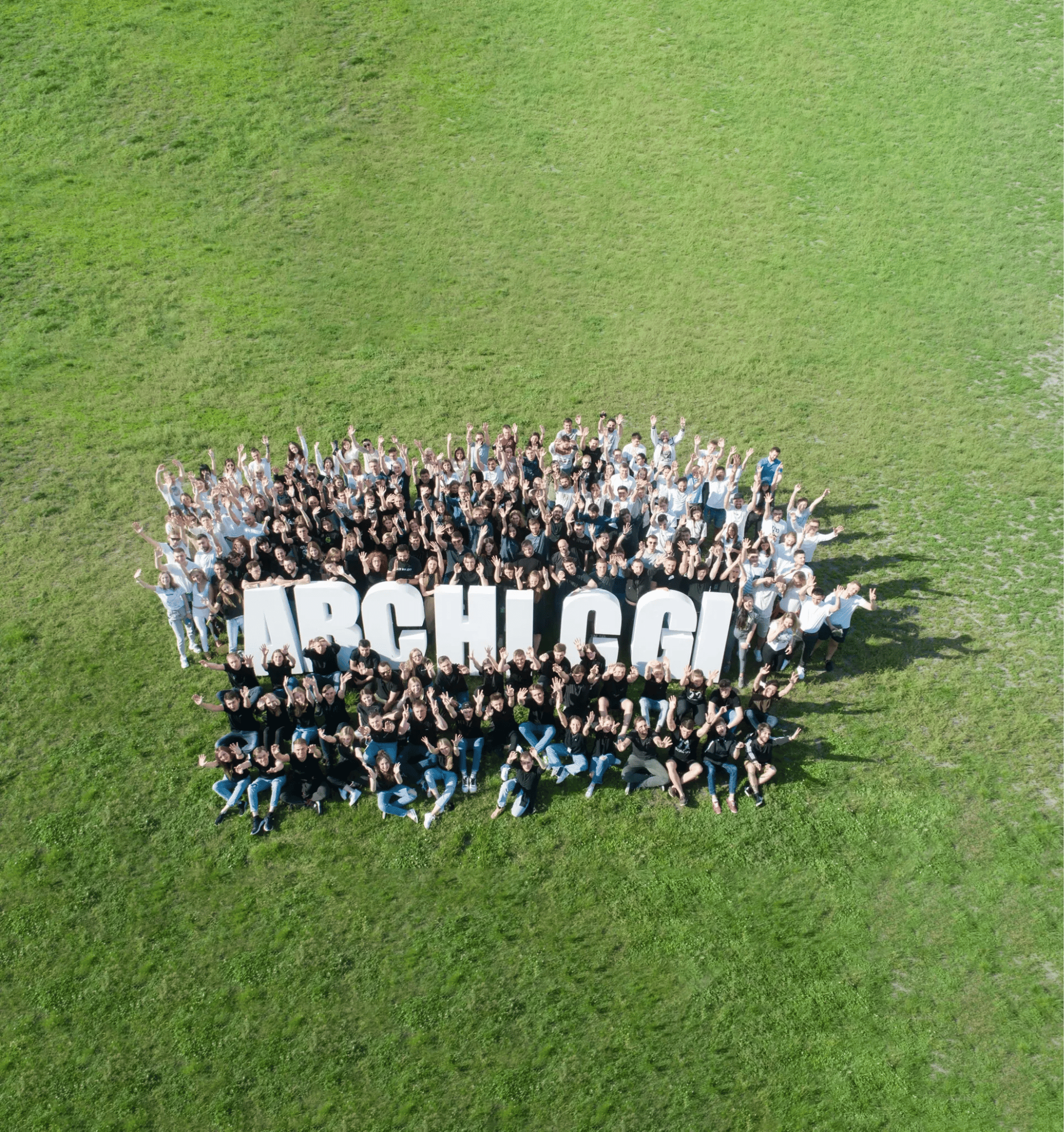 The ArchiCGI team lined up on a lawn to spell out the company name, seen from a drone