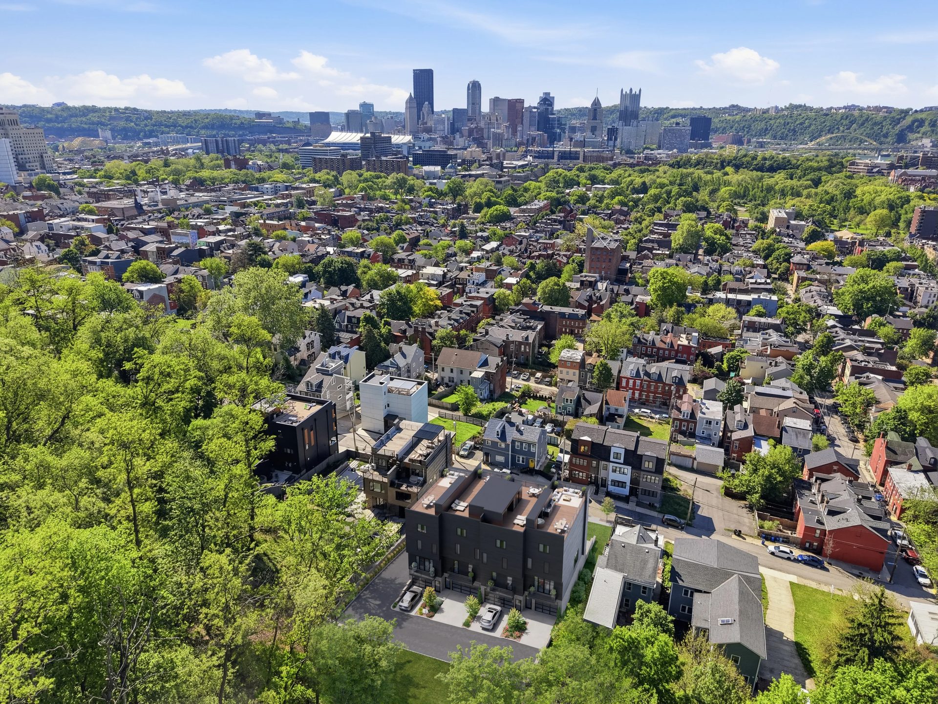 Aerial 3D render of modern townhouses composited into a Pittsburgh neighborhood with the downtown skyline in the background