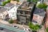 Architectural 3D visualization of a modern dark-clad multifamily building with glass facades, rooftop terrace, and balconies seen from an aerial perspective in an urban residential neighborhood